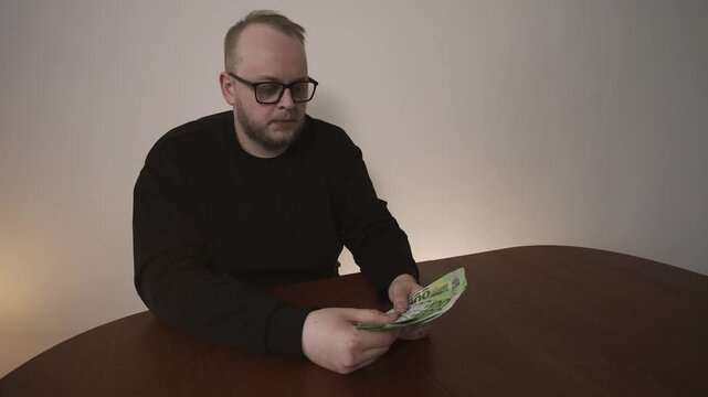 Young man shakes head in disappointment while counting euro banknotes. Low salary, financial dissatisfaction and personal budgeting stress.