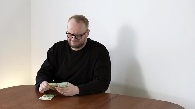 Male counts banknotes slowly with anxious expression, showing concern about finances and insufficient income. Concept of stress, budgeting, and uncertainty.