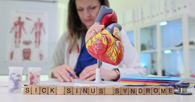 Wooden blocks spell phrase Sick Sinus Syndrome near heart model and stethoscope. Doctor writes ECG notes checking pulse rhythm while planning pacing