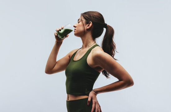 Woman in studio drinking green superfood drink after workout