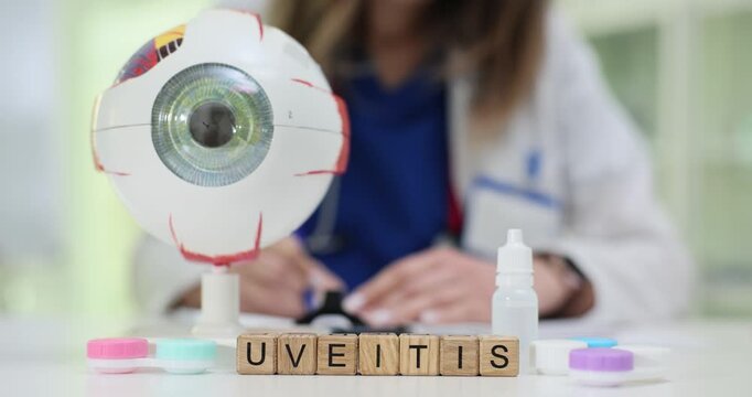 Wooden blocks spell word Uveitis near eyeball model and drops bottle. Doctor reviews symptoms prescribing eye drops and scheduling vision examination