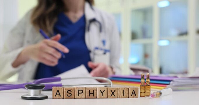 Wooden blocks spell word Asphyxia near ampoules and stethoscope on desk. Doctor writes emergency note checking airway steps while prepares rescue kit