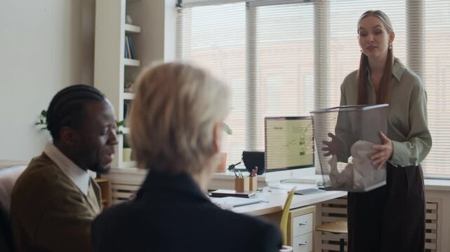 Over shoulder shot of diverse group of creative managers practicing stress relief at workplace in office, throwing papers into bin and joking