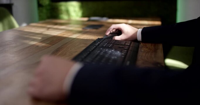 Close-up of a person in a business suit using a computer mouse and keyboard on a wooden desk