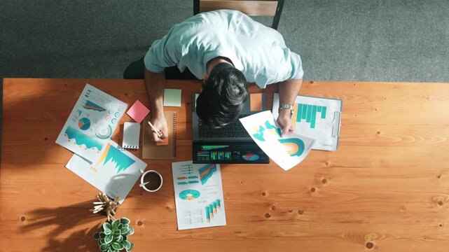 Top aerial view of manager working on laptop while looking at data analysis. Leader compare financial statistic graph while making decision at meeting table with document scatter around. Convocation.