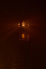 Warm light shining through tower windows in dense fog creates dramatic glowing rays and mysterious atmosphere. Moody night scene with soft haze and cinematic lighting, suitable for concepts of solitud © Ekaterina