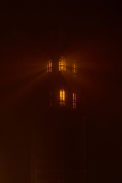 Warm light shining through tower windows in dense fog creates dramatic glowing rays and mysterious atmosphere. Moody night scene with soft haze and cinematic lighting, suitable for concepts of solitud