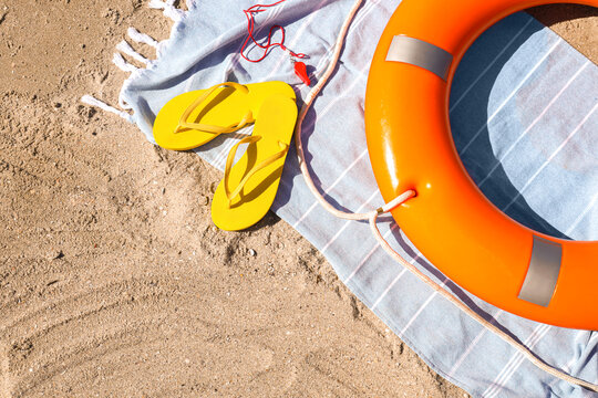 Lifebuoy ring with flip-flops, whistle and beach towel on sand