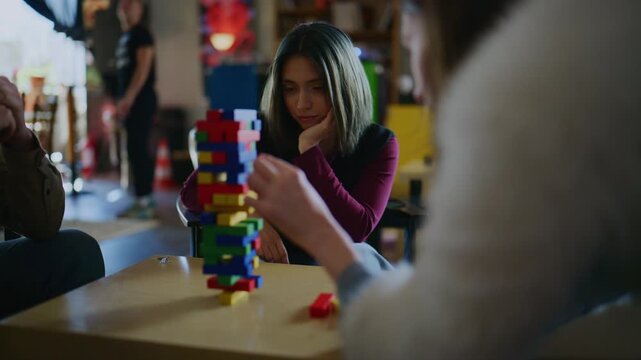 Two students are engrossed in a game of Jenga, carefully removing blocks from the tower. Friends enjoy a fun and challenging leisure activity together in a casual setting.
