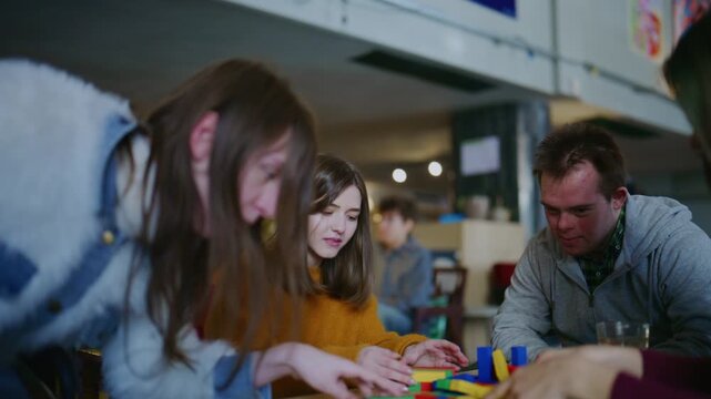Young students, including a person with Down syndrome, enjoy playing with colorful building blocks. They share smiles and positive interactions during their engaging and inclusive game session.