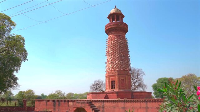 A wide static shot of the unique Hiran Minar tower, characterized by its stone elephant tusks and red sandstone construction, set against a clear sky in Fatehpur Sikri.