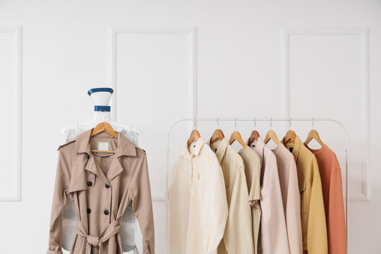 Modern steamer with coat and rack of stylish clothes on white background