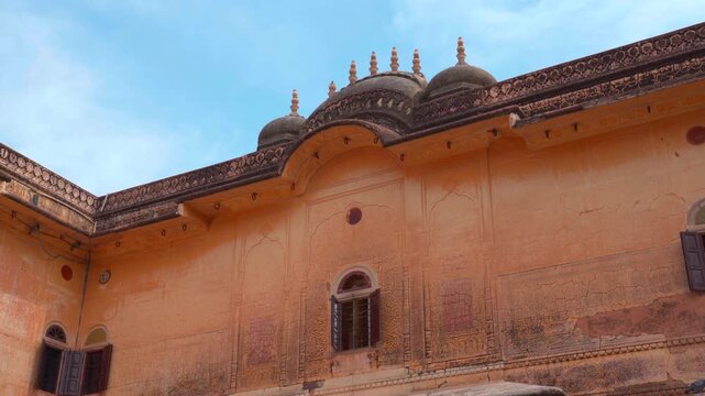 A static low-angle shot of the ornate upper facade of Nahargarh Fort, showcasing traditional Rajasthani domes, arched windows, and yellow sandstone walls against a clear blue sky.