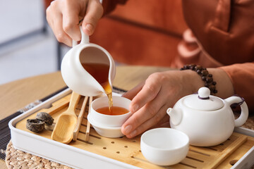 Asian woman pouring tea on table at home, closeup