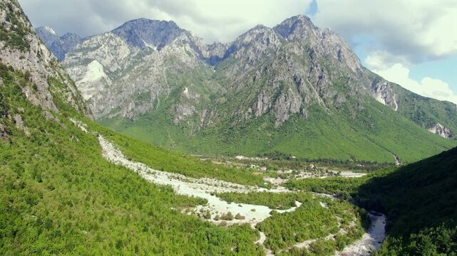 Scenic aerial view flying forward over the Theth Valley, a beautiful natural landscape with lush green forests and rugged mountains