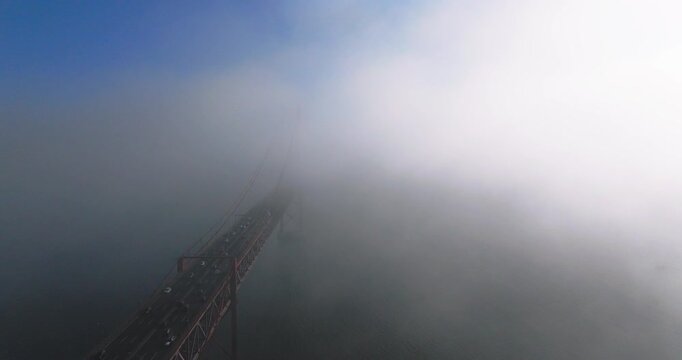 Cinematic aerial view of Lisbon&rsquo;s 25th April Bridge rising above a sea of clouds