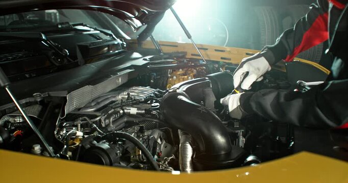 Slow motion shot of mechanic working on car engine with camera movement above engine, dramatic lighting in workshop. Automotive repair concept, maintenance and service.