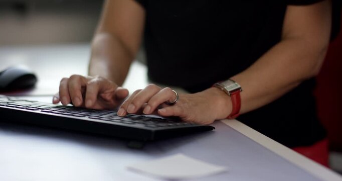 Close-up of a person with a wristwatch and ring typing on a black computer keyboard at a desk
