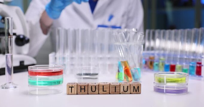 Word Thulium on wooden cubes against various color liquids in flasks on desk. Woman scientist conducts tests with samples in chemical laboratory