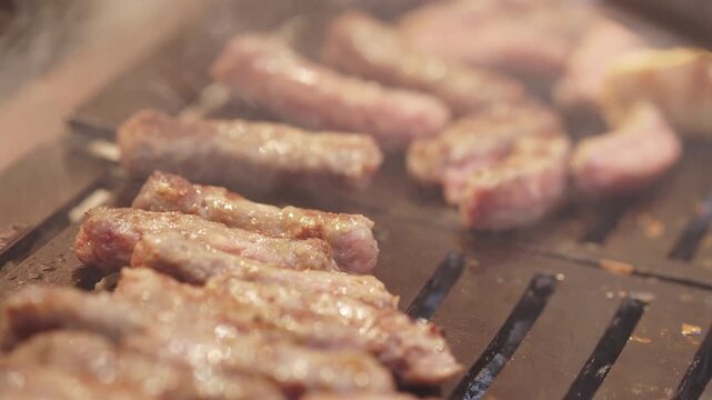 Grilling delicious minced meat kebabs on hot iron grill with steam rising in close motion.