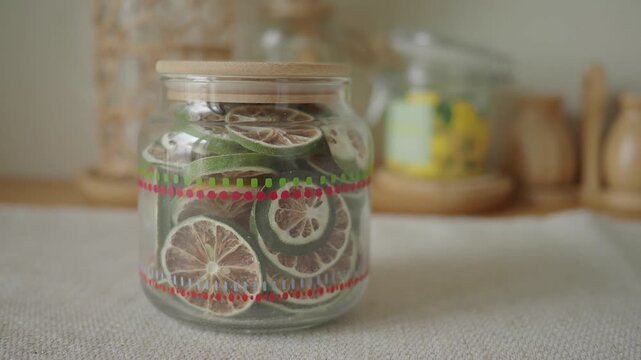 Close up of dried lime slices in glass jar with wooden lid on textured surface.