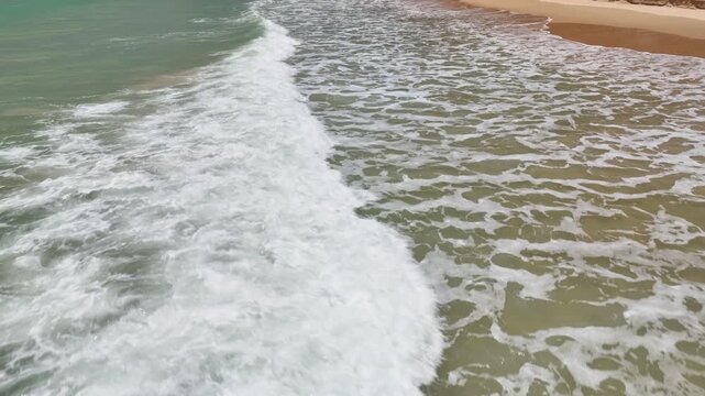 Aerial fly forward and rising camera up over sea  and wave crashing on beach
