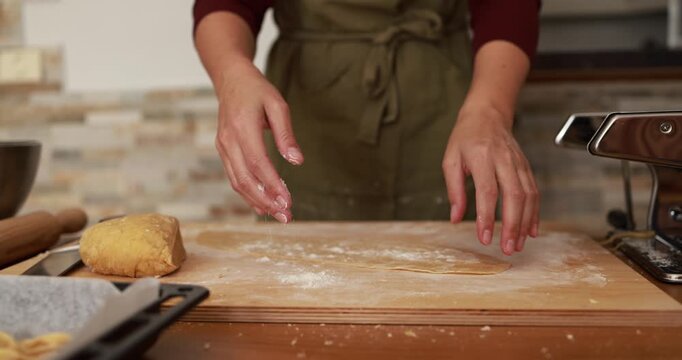 Young woman roll out the dough at home using pasta machine while preparing homemade tagliatelle - Healthy food and italian culture concept