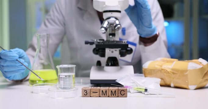 3-MMC inscription on wooden blocks with narcotics syringe and glassware in lab. Female scientist researches metaphedrone properties in laboratory