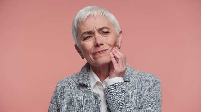 Senior woman suffering from tooth pain on pink