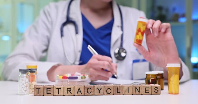 Wooden blocks spell word Tetracyclines near pill bottles on desk. Doctor writes prescription notes holding medicine container for dose guidance