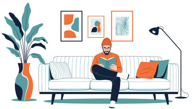 Young man with a beard and glasses sitting on a white sofa and reading a book in a stylish modern living room with art frames and a lamp.