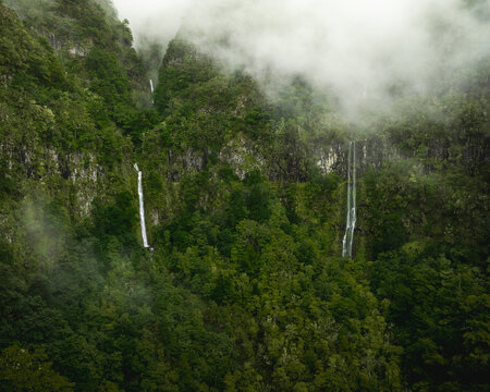 Aerial view of PR17 Pinaculo e Folhadal with waterfalls cascading down lush green cliffs shrouded in thick fog Serra de Agua, Madeira, Portugal.