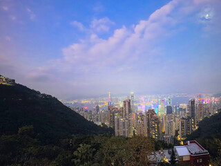 Obraz premium A breathtaking panoramic view of Victoria Peak captured while hiking uphill, showcasing the dense skyline of Hong Kong framed by lush tropical greenery.