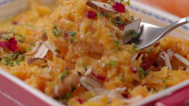 A close up view of delicious carrot halwa being served from baking dish into spoon.