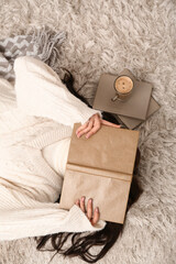 Naklejka premium Young woman with blanket, books and cup of coffee lying on floor at home, top view