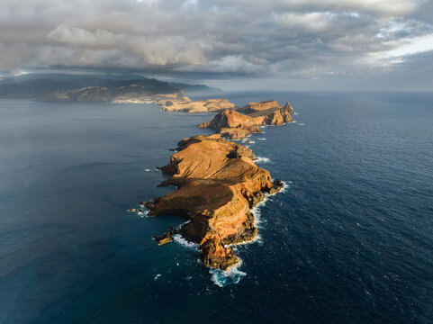 Aerial view of the rugged volcanic cliffs of Ponta de Sao Lourenco peninsula surrounded by the deep blue Atlantic Ocean under a cloudy sky in Canical, Madeira, Portugal.