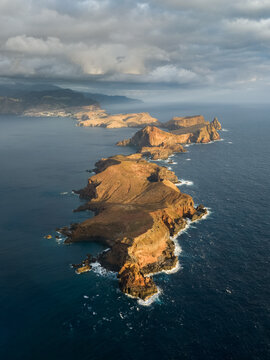 Aerial view of Ponta de Sao Lourenco peninsula with its rugged volcanic cliffs and rocky terrain surrounded by the deep blue Atlantic Ocean under a cloudy sky in Canical, Madeira, Portugal.