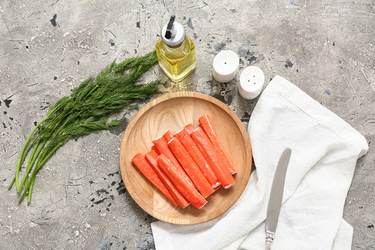 Wooden plate with tasty crab sticks and dill on grey background