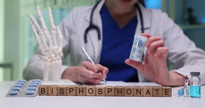 Wooden blocks spell word Bisphosphonate near hand bones model and tablets. Doctor reviews prescription monitoring bone protection plan daily