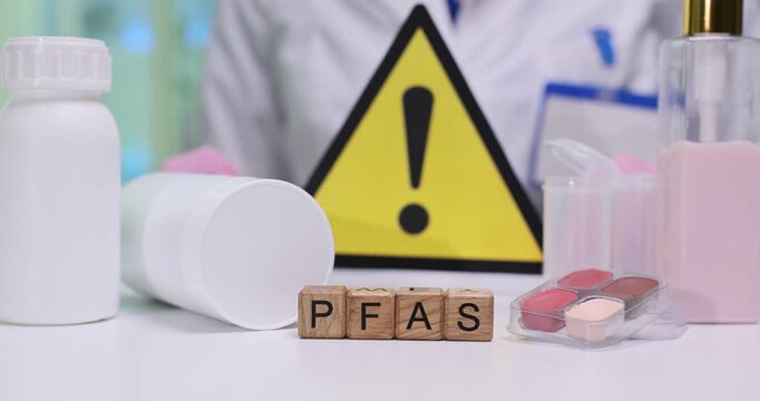 Wooden blocks spell abbreviation PFAS by bottles and warning sign. Scientist tests packaging sample recording contamination results for safety review
