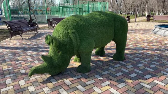 Green rhino topiary sculpture in public city park on paved plaza closeup camera zoom