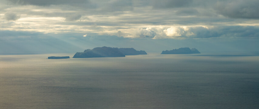Aerial view of the rugged cliffs of Ponta de Sao Lourenco and the Desertas Islands under a dramatic cloudy sky with sunbeams hitting the Atlantic Ocean in Canical, Madeira, Portugal.