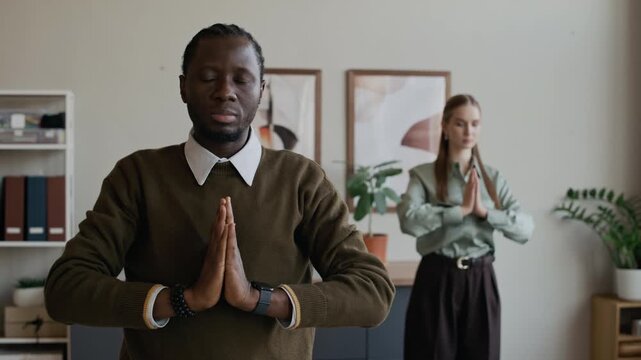 Medium shot of young Black man and Caucasian female colleague practicing yoga during break at work in office, perfect for burnout prevention and wellness concept