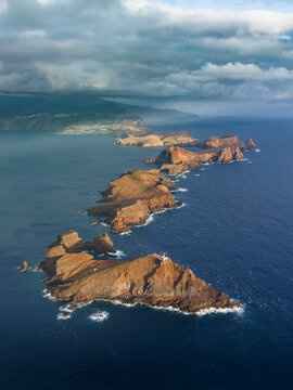 Aerial view of the rugged cliffs and volcanic rock formations of Ponta de Sao Lourenco peninsula stretching into the Atlantic Ocean under a dramatic cloudy sky in Canical, Madeira, Portugal.