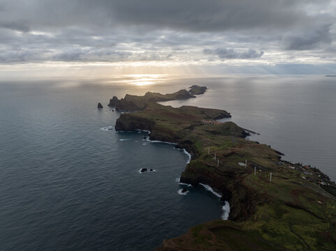 Aerial view of the rugged Ponta de Sao Lourenco peninsula with dramatic cliffs and wind turbines under a cloudy sky with sun rays in Canical, Madeira, Portugal.