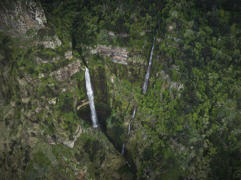 Aerial view of majestic waterfalls cascading down steep, lush green cliffs surrounded by dense forest in Canical, Madeira, Portugal.