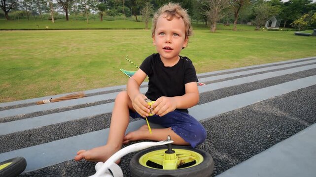 Little boy sits and plays with small tape measure, accidentally hitting his hand when it retracts suddenly. Toddler engaged with measuring tape, pulls it out and then lets go, causing it to snap back