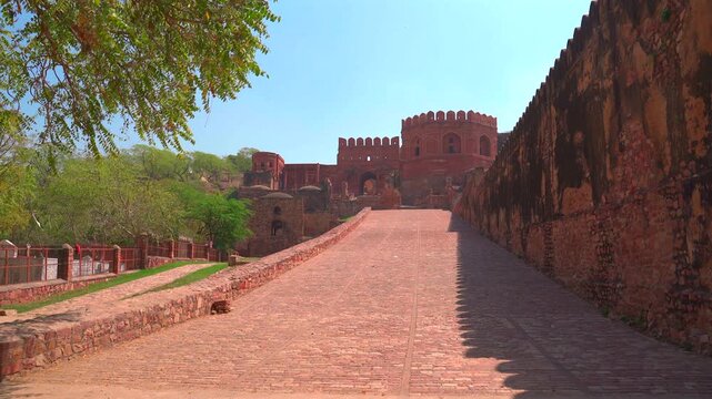 A wide static shot of the monumental red sandstone defensive walls and the stone-paved entrance ramp leading into the historic city of Fatehpur Sikri under a clear sky.