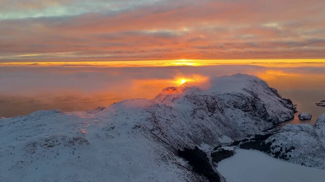 Breathtaking aerial view of a golden hour sunset over the snowcapped peaks of Lofoten, Norway, with clouds rolling through the valleys.