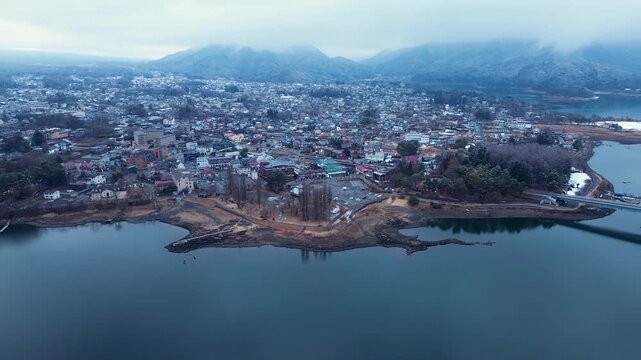 Drone aerial landscape of Fujikawaguchiko town village with suburban streets and commercial hotels next to lake with foggy forest mountains on the horizon in Yamanashi Japan Asia infrastructure travel